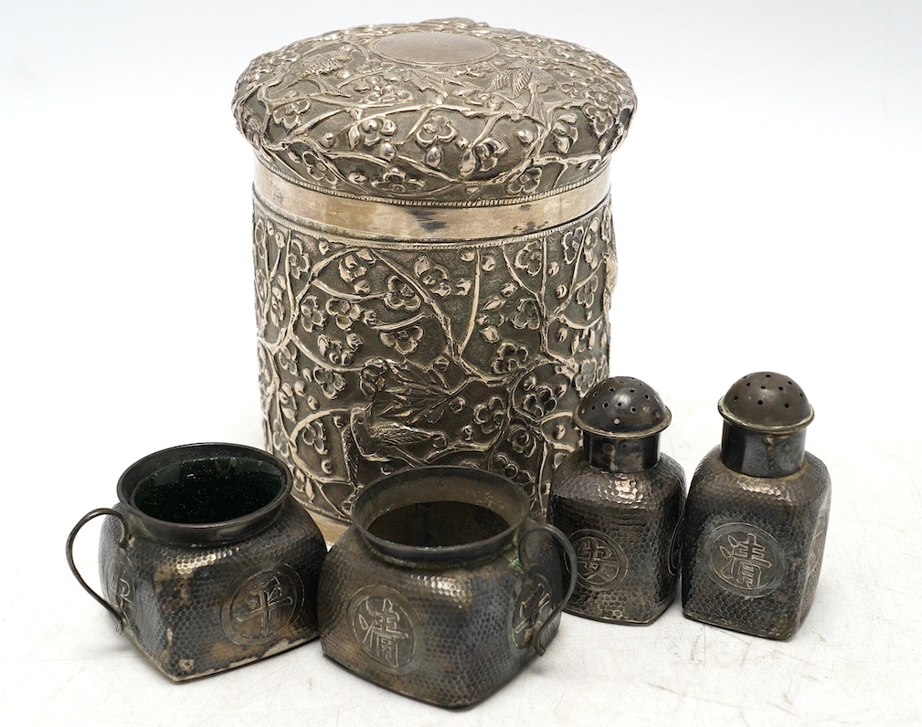 A Chinese embossed white metal cylindrical jar and cover, 11.2cm, and a similar white metal four piece cruet set. Condition - poor to fair